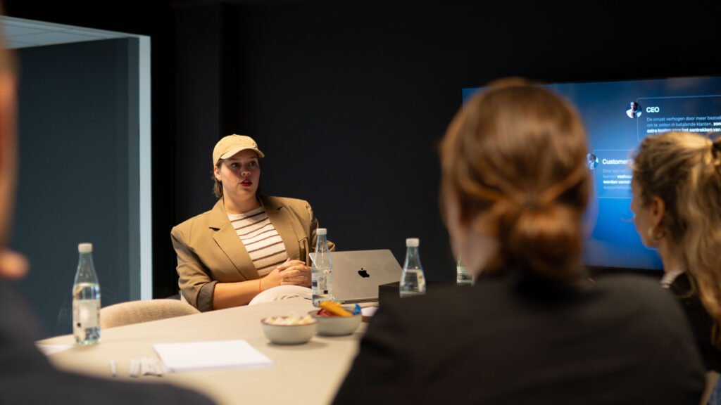 Vrouw geeft presentatie aan tafel met drie collega's en een scherm op de achtergrond