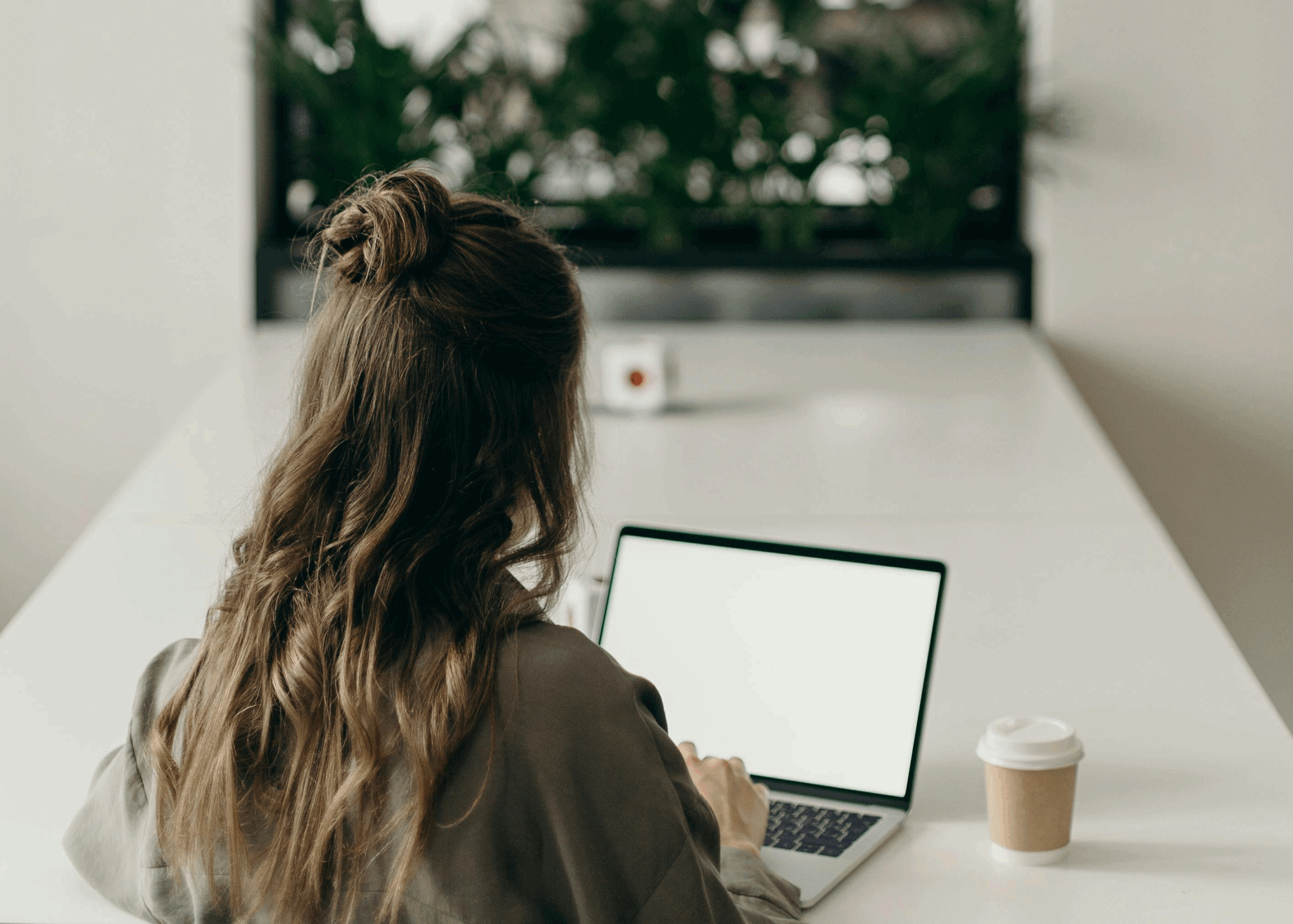 Vrouw zit achter laptop met een koffie to go beker - Klaviyo